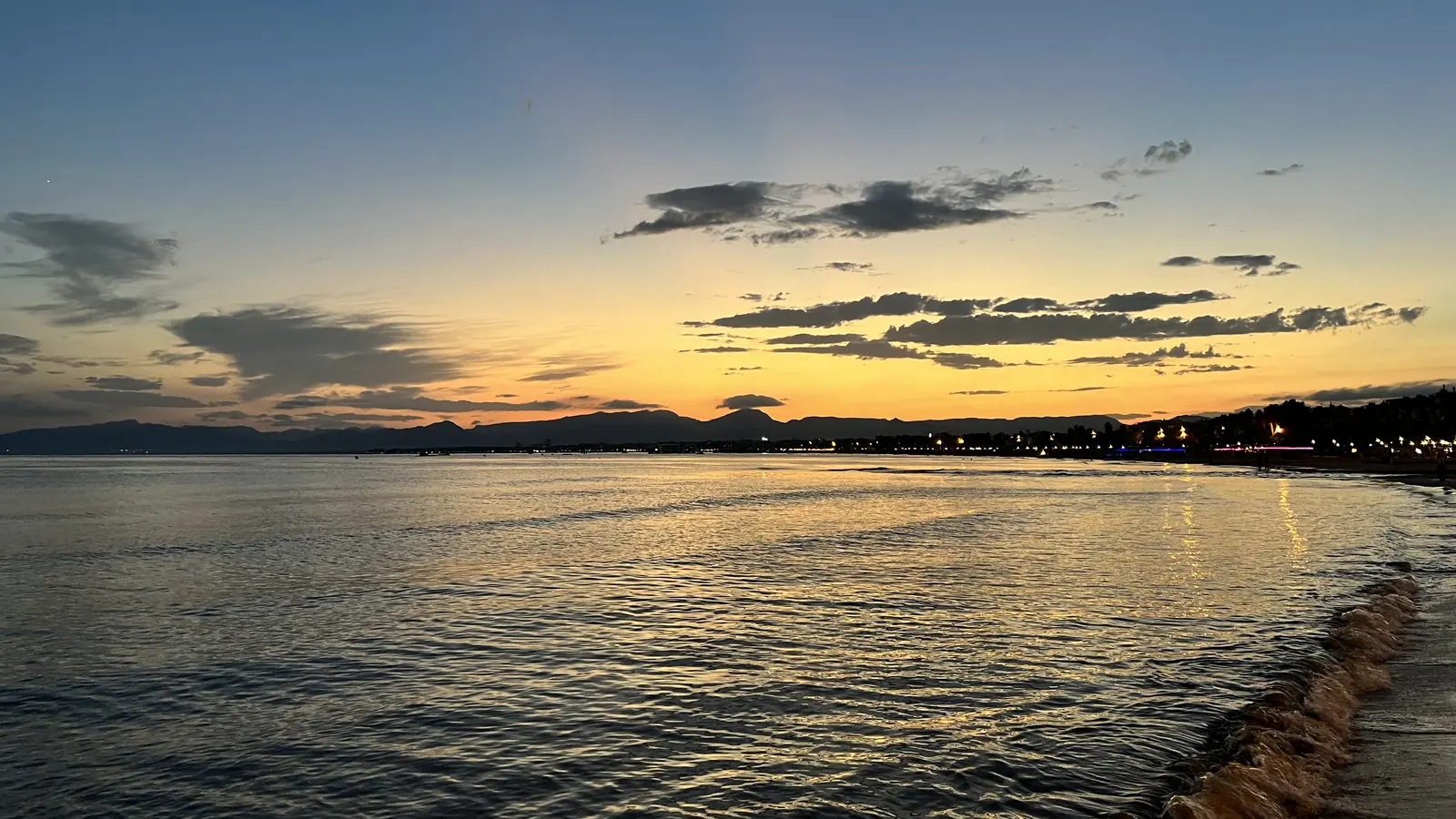 Dusk over the sea at Salou, with an orange and yellow sky above the calm water and the lit shoreline on the right